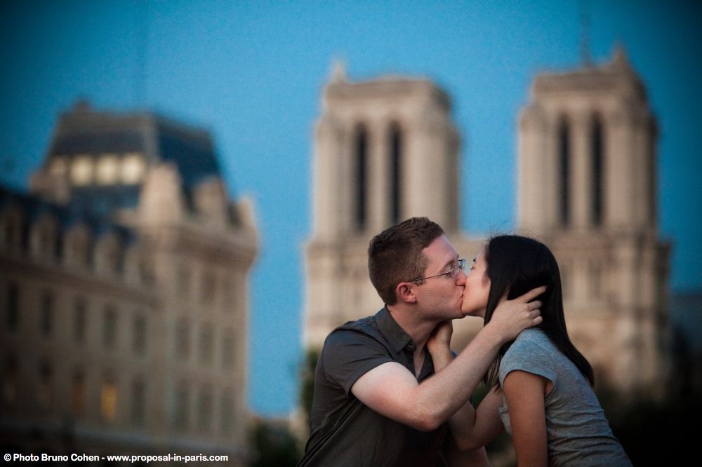 romantic portrait kissing couple from notre dame cathedral at sunrise in paris proposal
