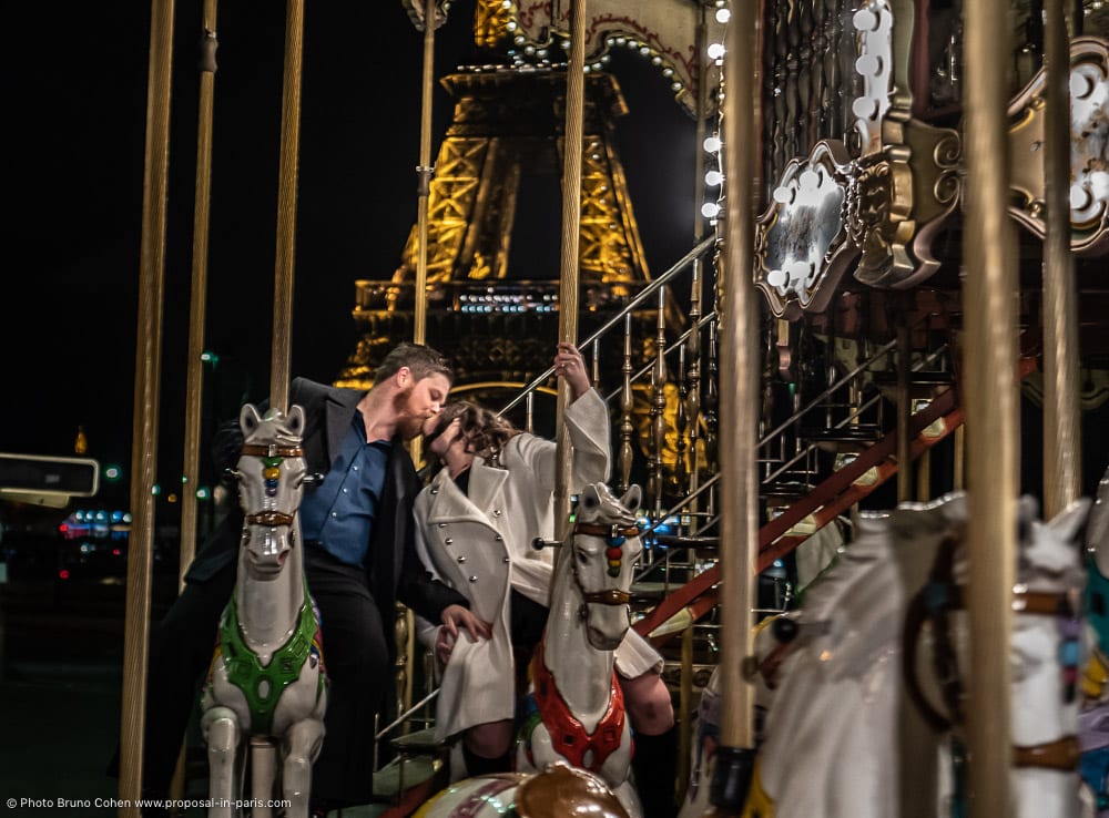 couple kiss riding a carousel horse in paris front Eiffel Tower at night