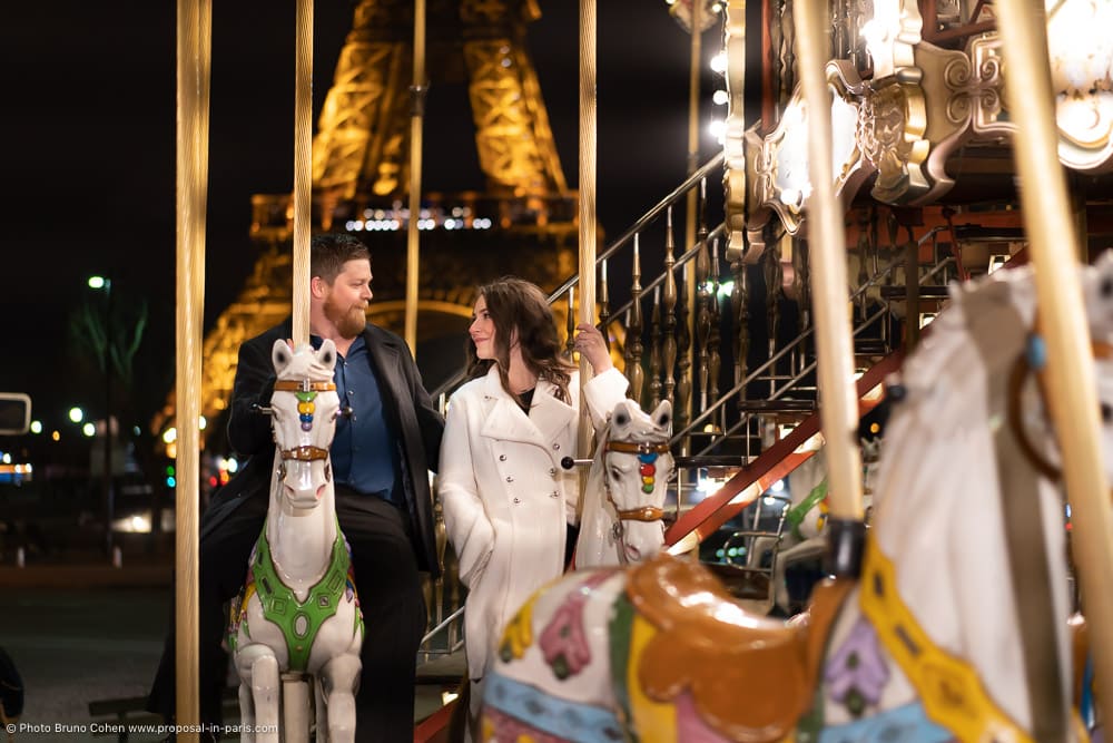 couple look at each other riding a carousel horse in paris front Eiffel Tower at night