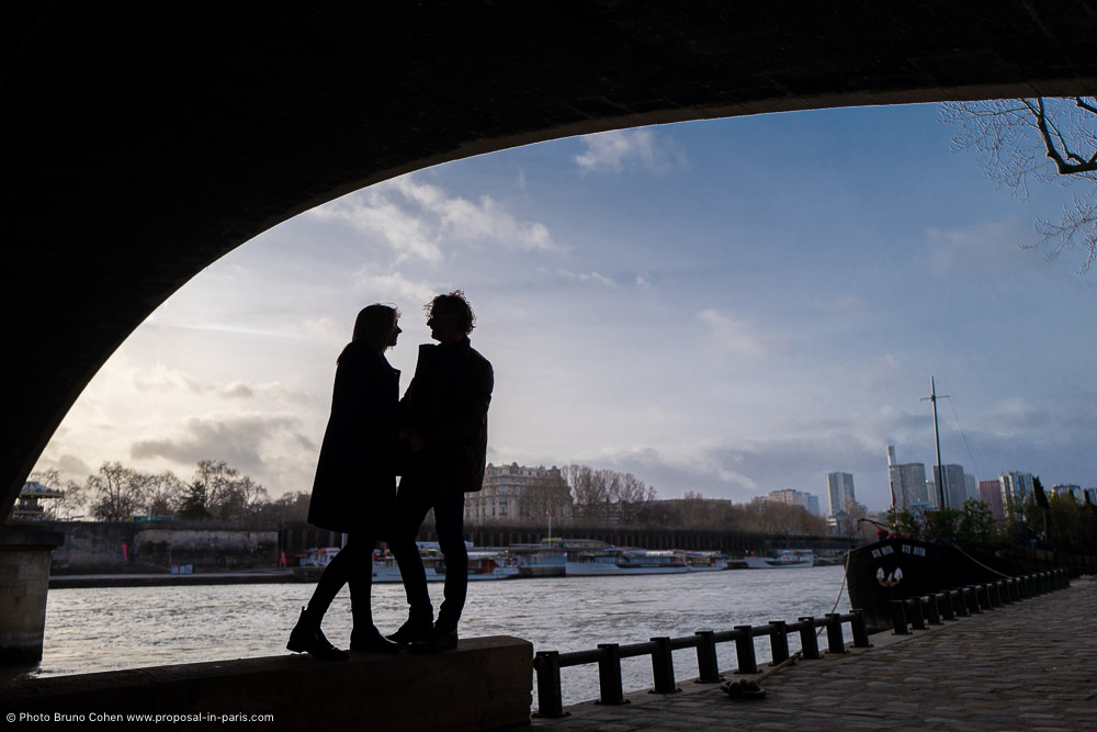 a couple look at each other under the bridge in paris