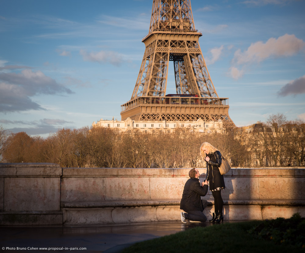 surprise proposal in paris at sunset from Bir Hakeim bridge front of Eiffel Tower couple in love emotions cry blue sky