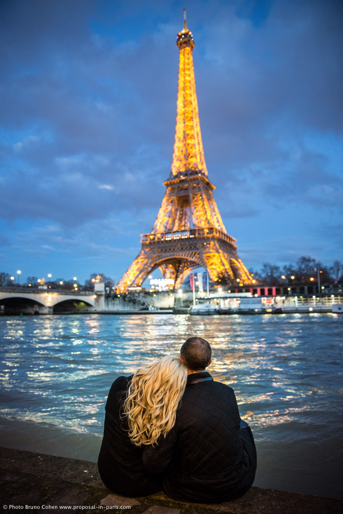 hugging couple look Eiffel Tower sparkles from seine banks at night