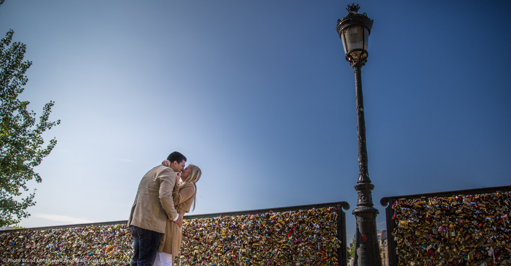 portrait kissing couple from lock bridge in paris summer proposal blue sky