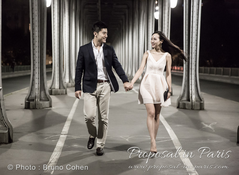 asian couple walking under Bir Hakeim bridge by night in paris 
