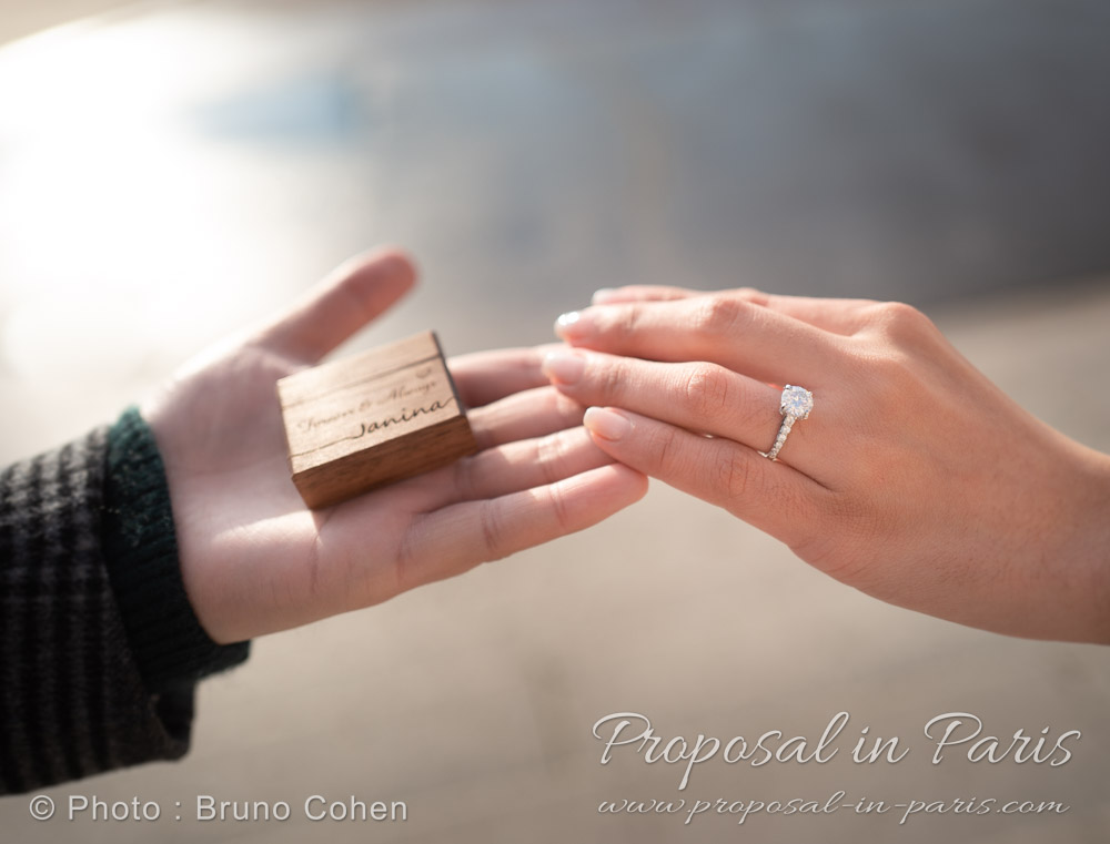two hands holding an engagement ring and a wooden box
