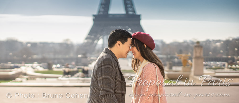 couple smiling and looking at each other, they are wearing coats. Eiffel Tower as backdrop. Sunrise