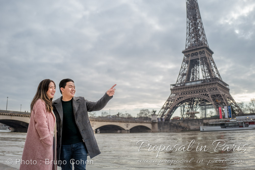 young asian couple in Paris, near the Eiffel Tower. He's showing something to her with his finger