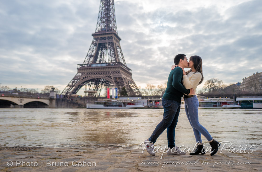 young couple kissing, standing up on the River Seine banks, with the Eiffel Tower behind them