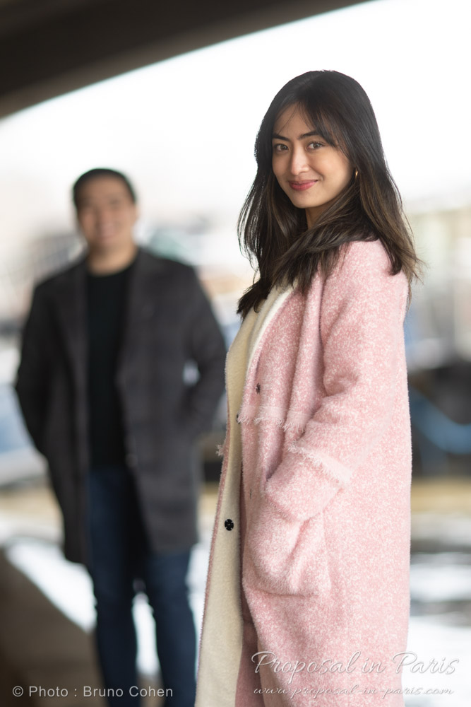 Young asian couple, she has a baby pink coat and look at the camera