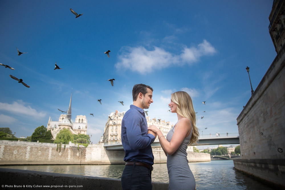 portrait couple face to face in love hand in hand from seine banks front of notre dame cathedral in paris summer proposal blue sky